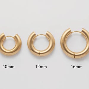 Könnte beinhalten: Drei goldene Creolen in verschiedenen Größen: 10 mm, 12 mm und 16 mm. Die Ohrringe sind glatt und haben eine polierte Oberfläche.