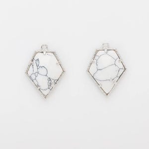 May include: Two white and silver gemstone pendants. Each pendant has a geometric shape with a white stone and a silver frame. The white stone has a black vein pattern. The pendants have a small loop at the top for hanging.