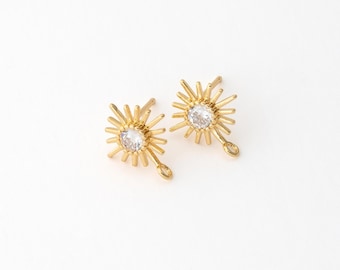 May include: Two gold-colored sunburst earrings with a central clear gemstone. The earrings have a detailed, spiky design radiating from the center stone. Each earring has a small loop at the bottom for attachment.