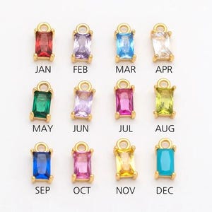 May include: A collection of twelve gold-colored rectangular charms, each featuring a different colored gemstone. Each charm is labeled with a month of the year: JAN, FEB, MAR, APR, MAY, JUN, JUL, AUG, SEP, OCT, NOV, and DEC. The gemstones are various colors.