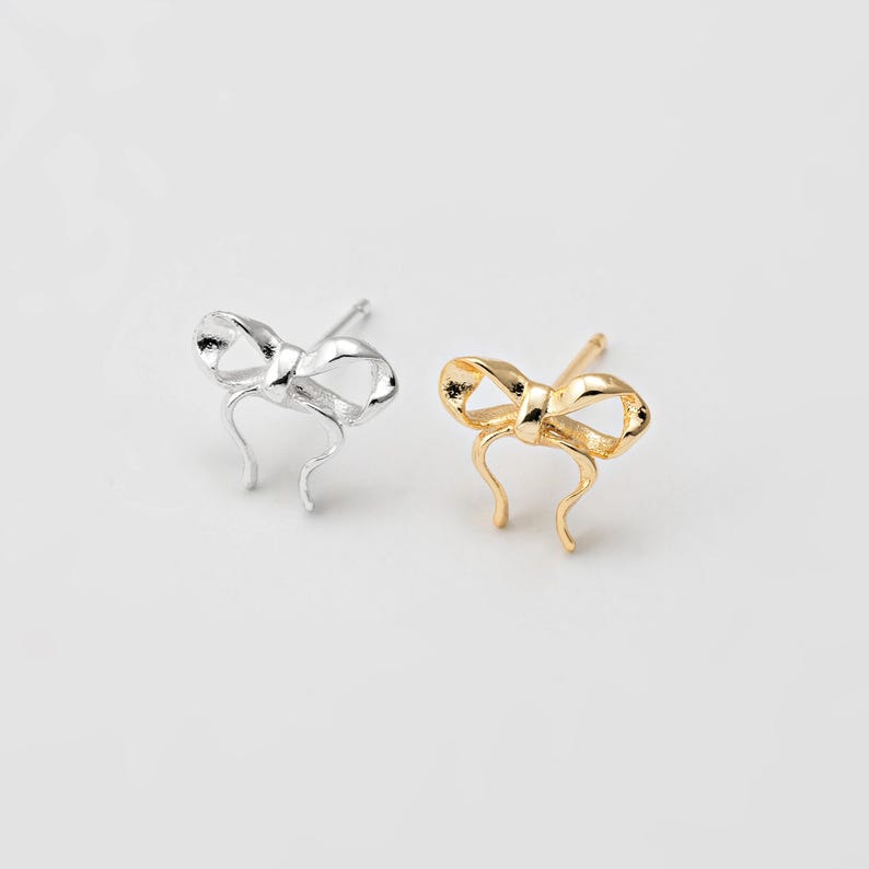 Op de afbeelding: Een paar oorringen in de vorm van een strik, een in zilver en een in goud.