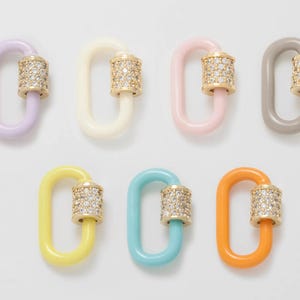 Può includere: Assortimento di charm link in smalto colorato e dorati con accenti di cristallo trasparente. I charm hanno la forma di un rettangolo con un bordo arrotondato e un piccolo anello su un lato. I charm sono disponibili in lavanda, bianco, rosa, grigio, giallo, blu e arancione.