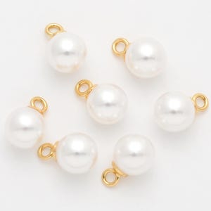 May include: Seven white pearl charms with gold-toned jump rings. The pearls are round and smooth.