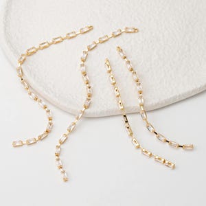May include: Gold-toned jewelry components featuring rectangular clear crystals. The components are arranged in a linear pattern, with small loops at the ends for attachment. The crystals are set in a gold-colored metal.