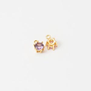 May include: Two gold-tone charms with a purple rhinestone in the center. The charms have a loop at the top for attaching to a necklace or bracelet.