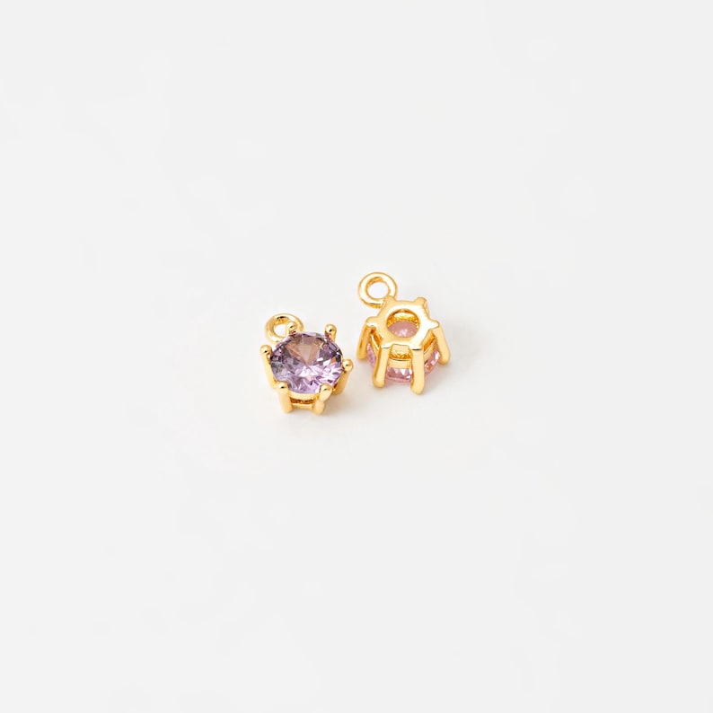 May include: Two gold-tone charms with a purple rhinestone in the center. The charms have a loop at the top for attaching to a necklace or bracelet.