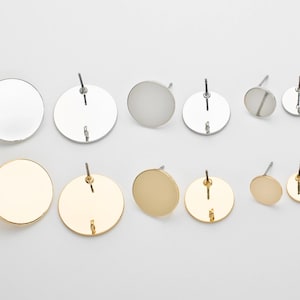 May include: A set of eight round stud earrings in silver and gold tones. The earrings are all different sizes and have a smooth, polished finish.