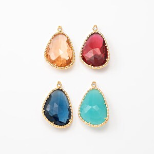 May include: Four gemstone pendants in shades of orange, red, blue, and turquoise. Each pendant has a gold-colored bezel with a small crystal at the top. The pendants are teardrop-shaped and have a faceted surface.