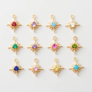 May include: Twelve gold starburst charms with different colored gemstones in the center. The charms are perfect for jewelry making or adding a touch of sparkle to crafts.