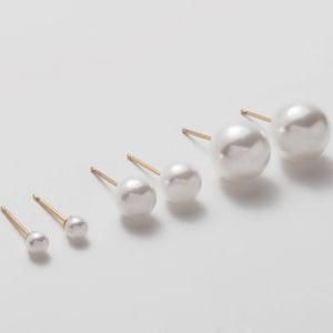 Puede incluir: Conjunto de seis pendientes de botón de perla en varios tamaños, con postes de oro. Los pendientes están dispuestos en una línea del más pequeño al más grande.