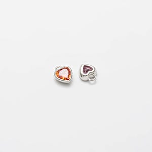 May include: Two silver heart-shaped charms with a red and orange gemstone in each.