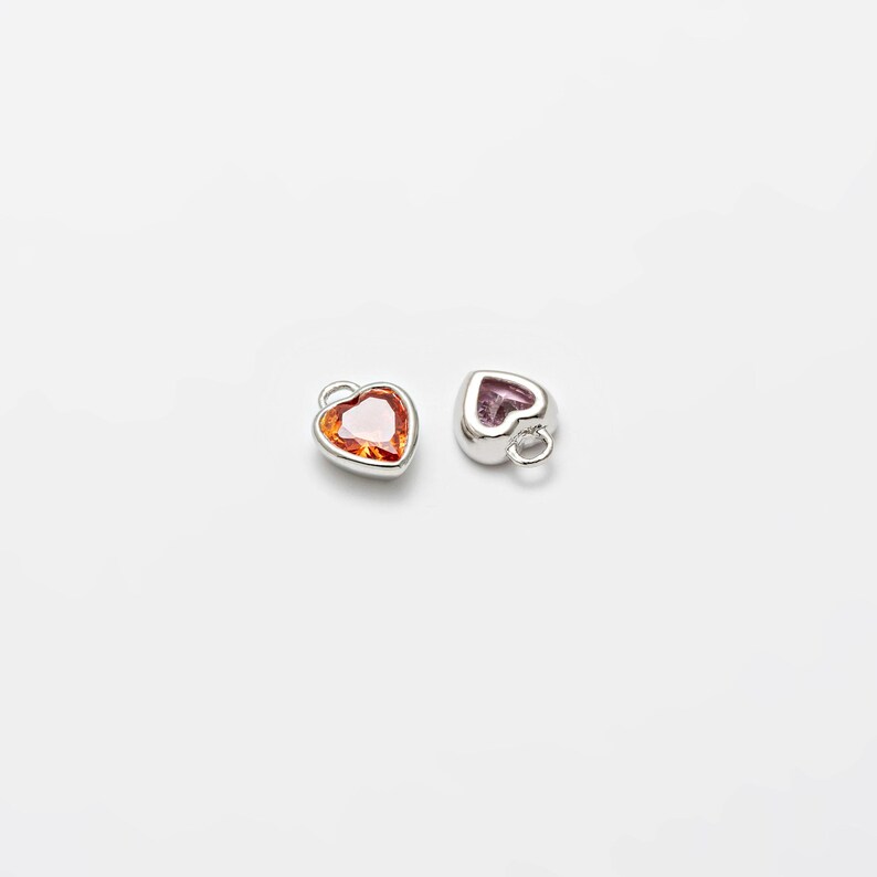 May include: Two silver heart-shaped charms with a red and orange gemstone in each.