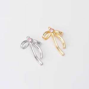 May include: Two gold and silver bow charms with pink rhinestones. The charms are in the shape of a bow with two long tails.