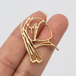 Op de afbeelding: Een goudkleurige metalen hanger in de vorm van een gestileerd vrouwenprofiel. De hanger heeft een lus aan de bovenkant om op te hangen en heeft ingewikkelde uitgesneden details. Het ontwerp is elegant en geschikt voor het maken van sieraden.