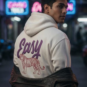 May include: Cream-colored hoodie with the word "Easy" in purple script and a tiger graphic. The hoodie is worn with a black leather jacket. The background features neon signs and a city street.