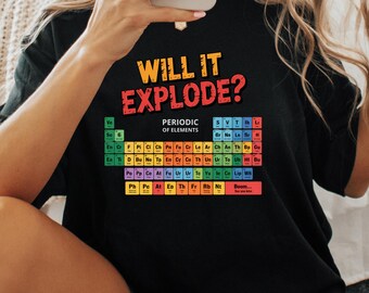 May include: Black t-shirt with the text "WILL IT EXPLODE?" in yellow and red. Below the text is a colorful periodic table of elements. The shirt is a science-themed graphic tee.