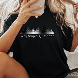 May include: Black t-shirt with a white graphic design of a sound wave and the text "Why Stupid, Question?" The shirt is made of a soft material.