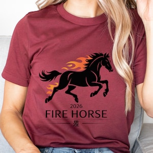 May include: Burgundy t-shirt with a black horse design and orange flames. The text "2026 FIRE HORSE" is below the horse, with Chinese characters beneath. The shirt is a solid burgundy colour.
