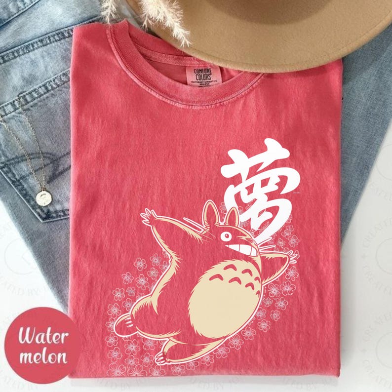 May include: A red t-shirt with a cartoon character and the Japanese word for "dream" in white. The character is surrounded by small white flowers. The shirt is labelled "Watermelon".