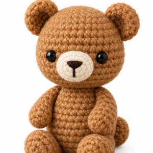 Peut inclure: Un petit ours en peluche crocheté en fil marron clair avec un museau de couleur crème. L'animal en peluche présente deux yeux ronds en plastique noir et un nez brodé marron foncé. Il est assis en position verticale avec des mailles visibles.