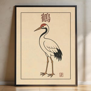 以下が含まれることがあります： 赤い頭と黒い模様のある白い鶴の黒枠プリント。鶴はベージュの背景に立っており、その上に赤い鶴の漢字が書かれており、右下に赤いスタンプが押されています。
