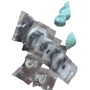 May include: A collection of seahorse and seashell-themed cabinet hardware. The seahorse pulls are dark gray, and the seashell knobs are a light turquoise. The hardware is packaged in clear plastic bags with white labels.