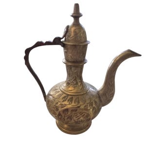 May include: A vintage brass pitcher with a long spout, curved handle, and ornate floral engravings. The pitcher has a bulbous body and a decorative lid. The overall design is detailed and elegant, suggesting a decorative or ceremonial purpose.