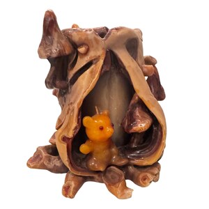 May include: A carved candle holder in shades of brown and tan, shaped like a tree trunk with a small, orange teddy bear candle inside. The bear has red eyes and a small wick.