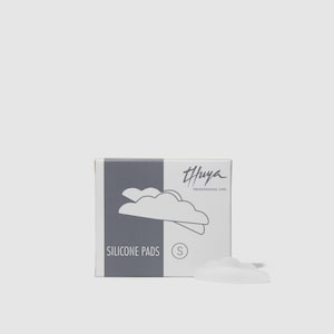 Puede incluir: Una caja de almohadillas de silicona Thuya Professional Line, talla S, con un gráfico en forma de nube. La caja es blanca y gris, con el nombre de la marca y la descripción del producto impresos. Una sola almohadilla de silicona blanca está al lado de la caja.