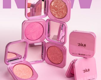 May include: Pink blush compacts with mirrors are displayed against a pink background. The compacts are open, revealing the blush colors, and the text "ZOLA" and "VELVETBLUSHGLOW" are visible. The word "NEW" is in the background.