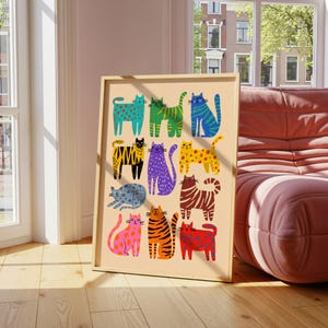 May include: A framed art print featuring a collection of colorful, stylized cat illustrations. Each cat is uniquely patterned with spots, stripes, and various colors, including blue, green, yellow, and orange. The artwork is displayed in a light-colored wooden frame.