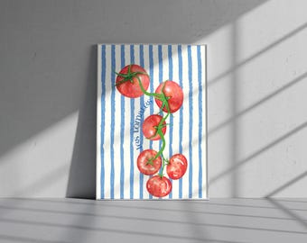 Op de afbeelding: Een ingelijste aquarelprint met een tros rijpe rode tomaten met groene stelen tegen een achtergrond van blauwe en witte verticale strepen. De woorden "les tomates" zijn in het blauw geschreven.
