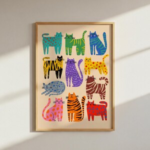 May include: A framed art print featuring a collection of colorful, stylized cat illustrations. The cats are depicted in various poses and patterns, including polka dots, stripes, and solid colors, against a beige background. The artwork is framed in a light wood frame.