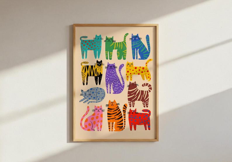 May include: A framed art print featuring a collection of colorful, stylized cat illustrations. The cats are depicted in various poses and patterns, including polka dots, stripes, and solid colors, against a beige background. The artwork is framed in a light wood frame.