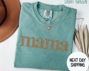 May include: Light green t-shirt with the word "mama" embroidered in a floral design. A silver necklace with a pendant rests on the shirt. The text "LIGHT GREEN" is at the top, and "NEXT DAY SHIPPING" is at the bottom.