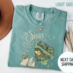 May include: Light green t-shirt with a graphic of a hobbit house and the text "The Shire" and a quote from the book "The Hobbit".