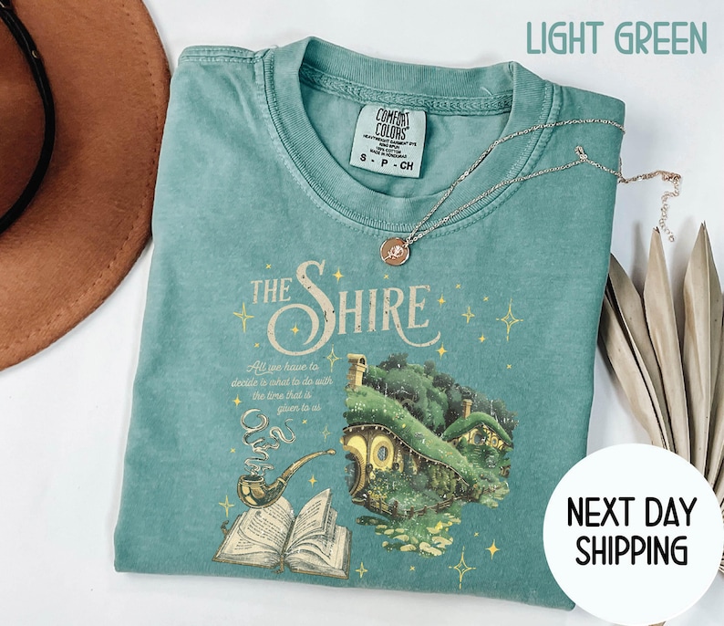 May include: Light green t-shirt with a graphic of a hobbit house and the text "The Shire" and a quote from the book "The Hobbit".