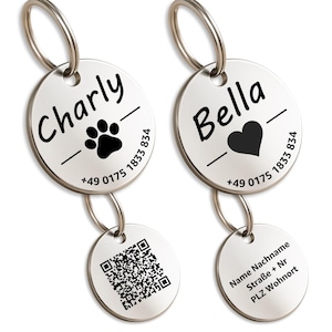 Könnte beinhalten: Zwei silberne Hunde-ID-Marken. Eine Marke hat den Namen "Charly" mit einem Pfotenabdruck, die andere "Bella" mit einem Herzen. Beide haben eine Telefonnummer. Zusätzliche Marken haben einen QR-Code und Informationen zum Besitzer.