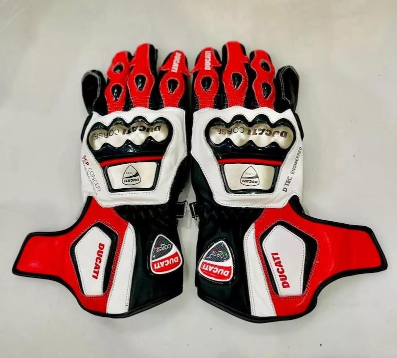 May include: A pair of black, white, and red motorcycle gloves with the Ducati Corse logo. The gloves have a D-Tec engineered design and are made of leather.