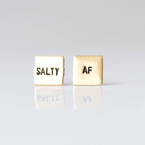 May include: A pair of gold-toned earrings with the words "SALTY" and "AF" engraved on them.