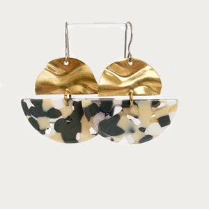 Peut inclure: Une paire de boucles d'oreilles statement dorées et blanches avec un dessus en or texturé et un bas marbré noir et blanc.