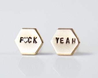 May include: A pair of gold hexagonal stud earrings with the words "F**K" and "YEAH" engraved on them.