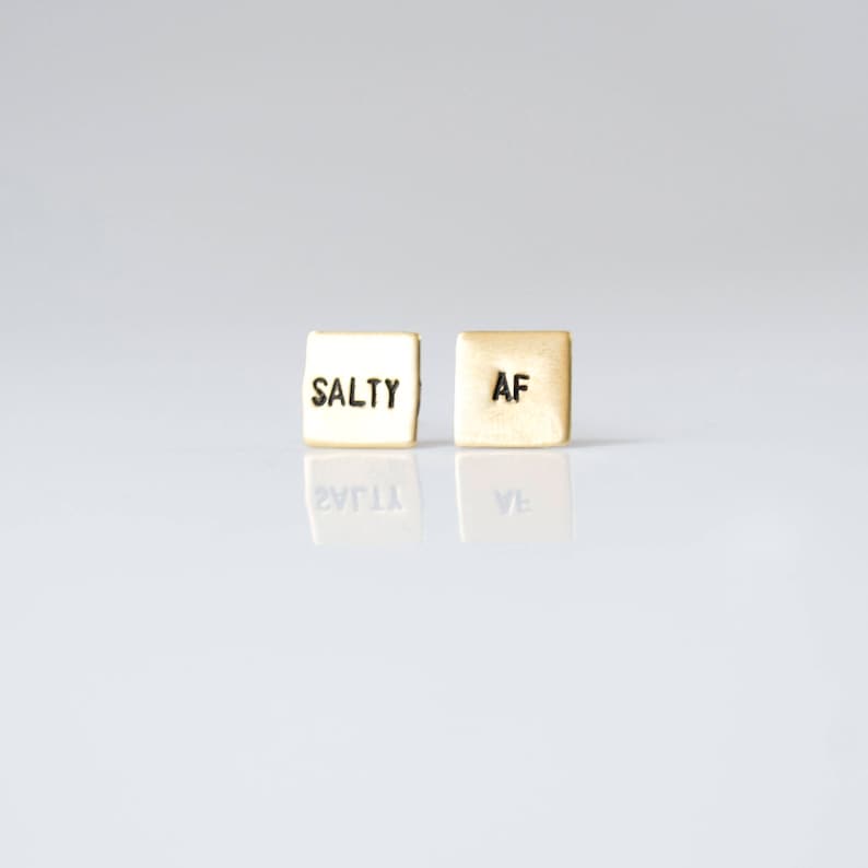 May include: A pair of gold-toned earrings with the words "SALTY" and "AF" engraved on them.