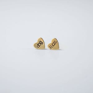 May include: A pair of gold heart-shaped earrings with the words "dog" and "mom" engraved on them.