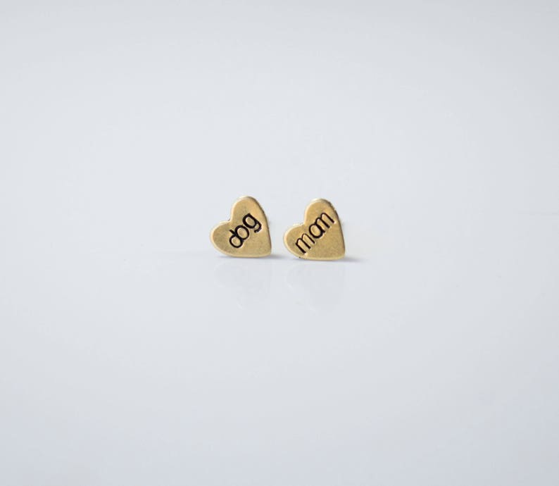May include: A pair of gold heart-shaped earrings with the words "dog" and "mom" engraved on them.