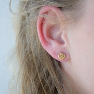 May include: Gold stud earrings with the word "omg" engraved on the front.