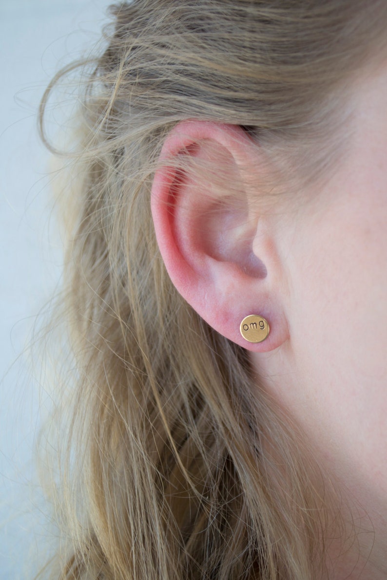 May include: Gold stud earrings with the word "omg" engraved on the front.