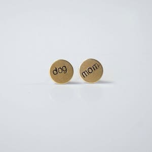 May include: A pair of gold-toned earrings with the words "dog" and "mom" engraved on them.
