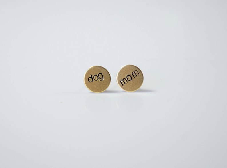 May include: A pair of gold-toned earrings with the words "dog" and "mom" engraved on them.