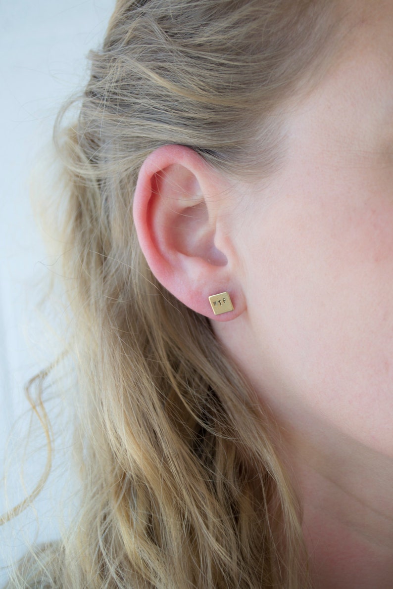 May include: A close-up of a person's ear with a small gold square earring that says "WTF" on it.